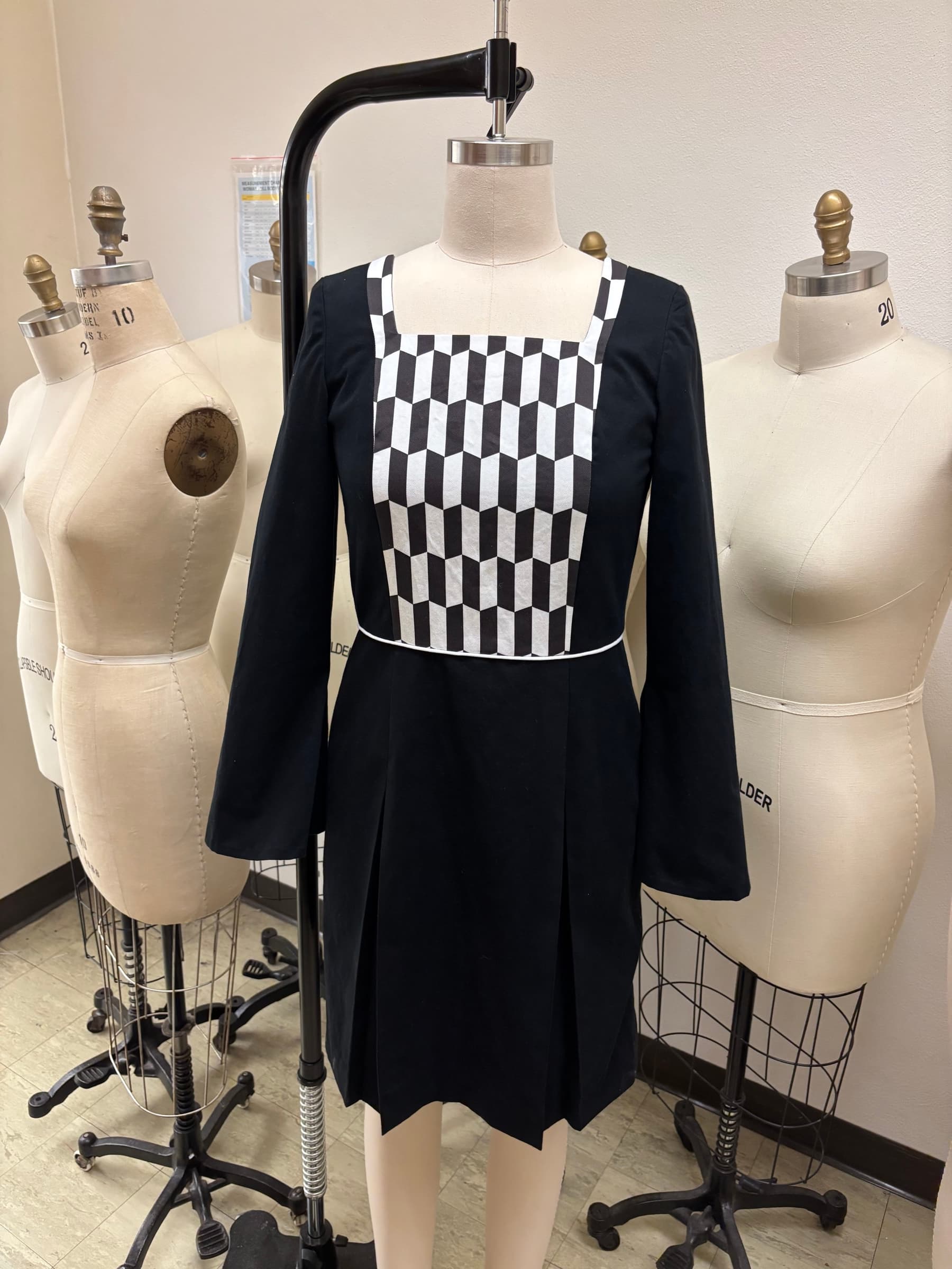 Black long-sleeved dress with a geometric black and white cube-print bib panel, on a dress form