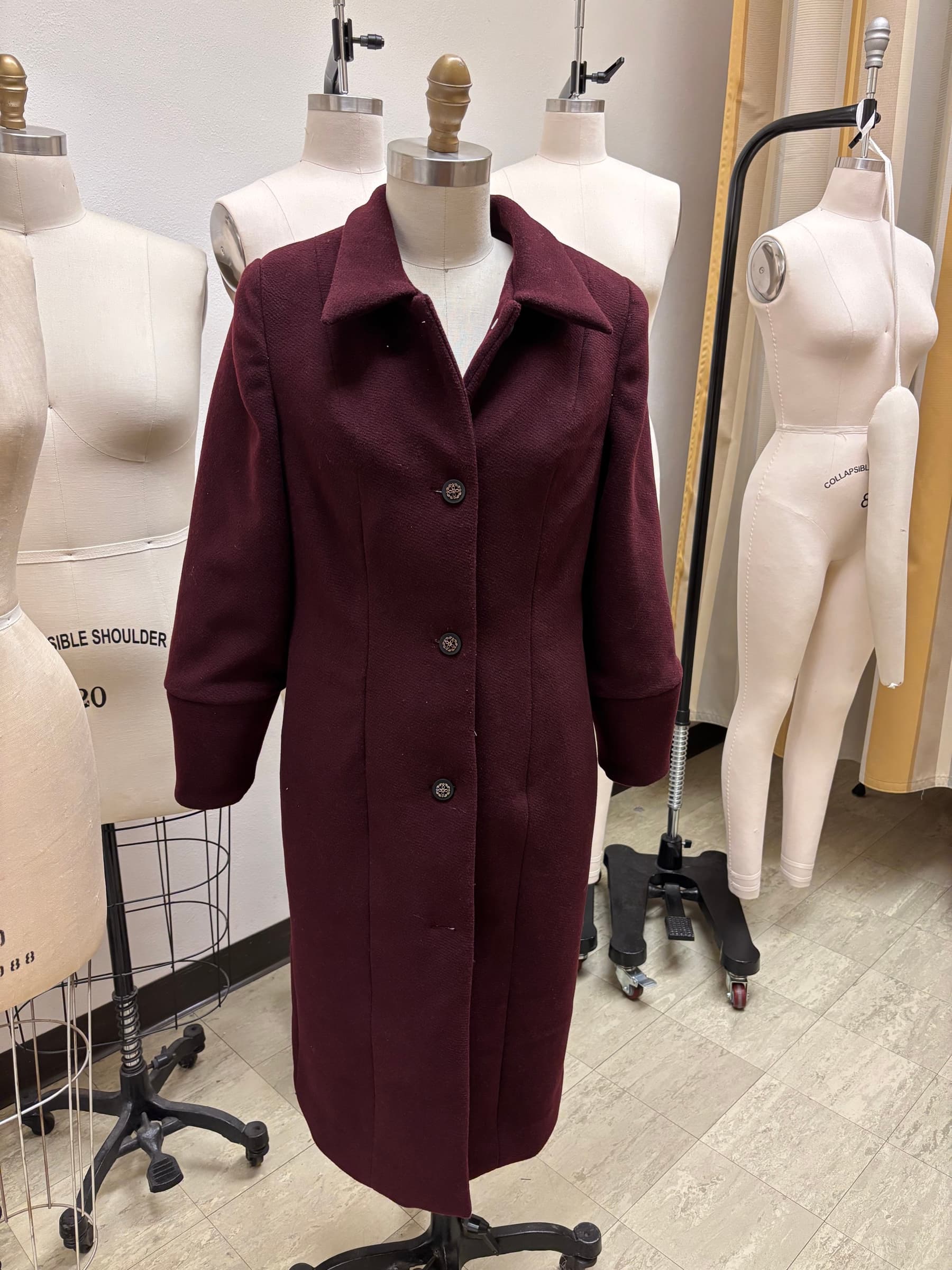 Full-length burgundy wool coat with a pointed collar and covered buttons, on a dress form